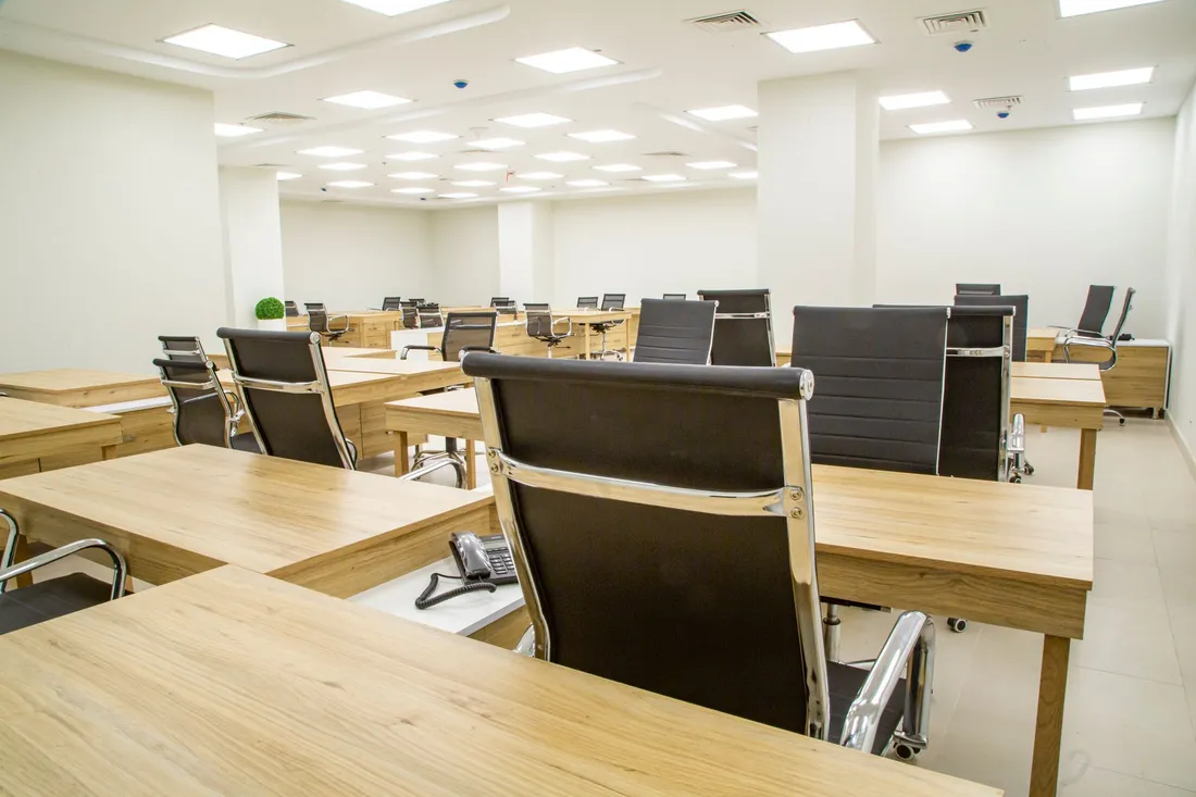 Leeres Großraumbüro mit Reihen heller Holzschreibtische, schwarzen Bürostühlen und einem Tischtelefon