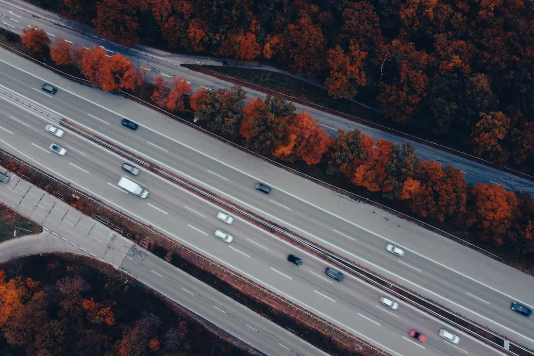 Luftaufnahme einer mehrspurigen Autobahn mit fahrenden Autos zwischen herbstlich rot gefärbten Bäumen