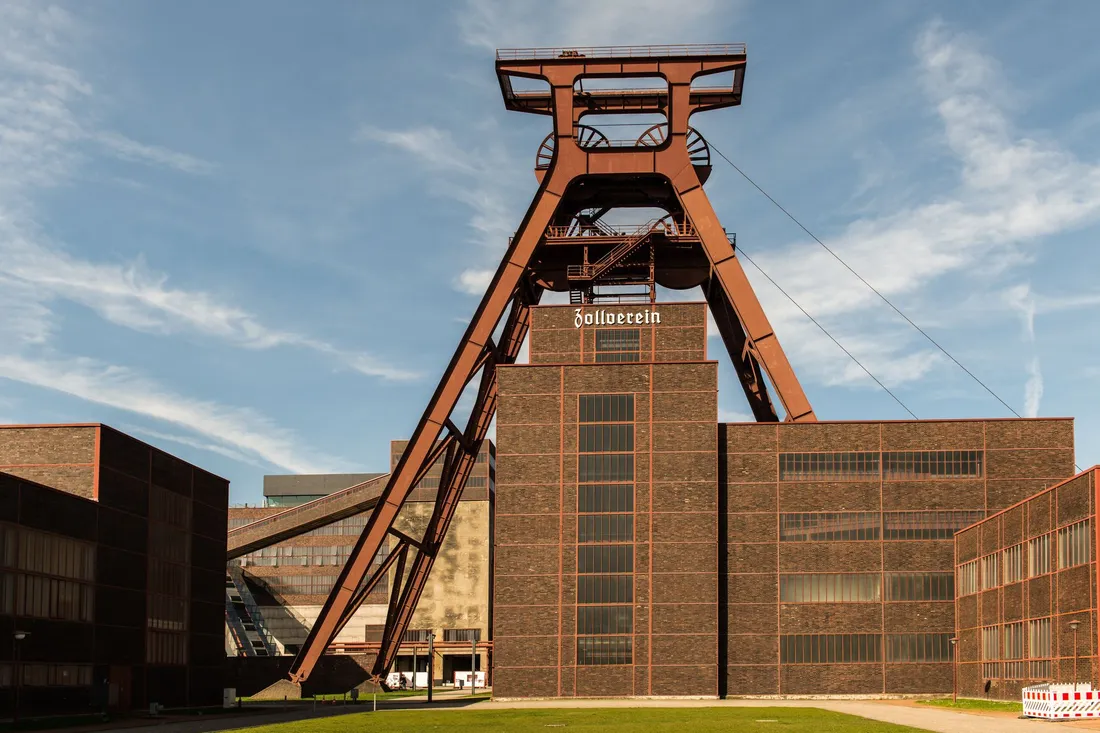 Rostrotes Doppelbock-Fördergerüst über dunklen Backsteinbauten der Zeche Zollverein