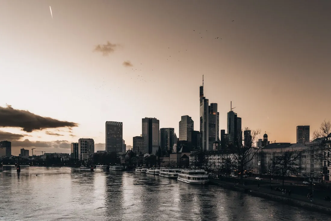 Hochhaus-Skyline im Abendlicht hinter einem Fluss mit angelegten Ausflugsschiffen