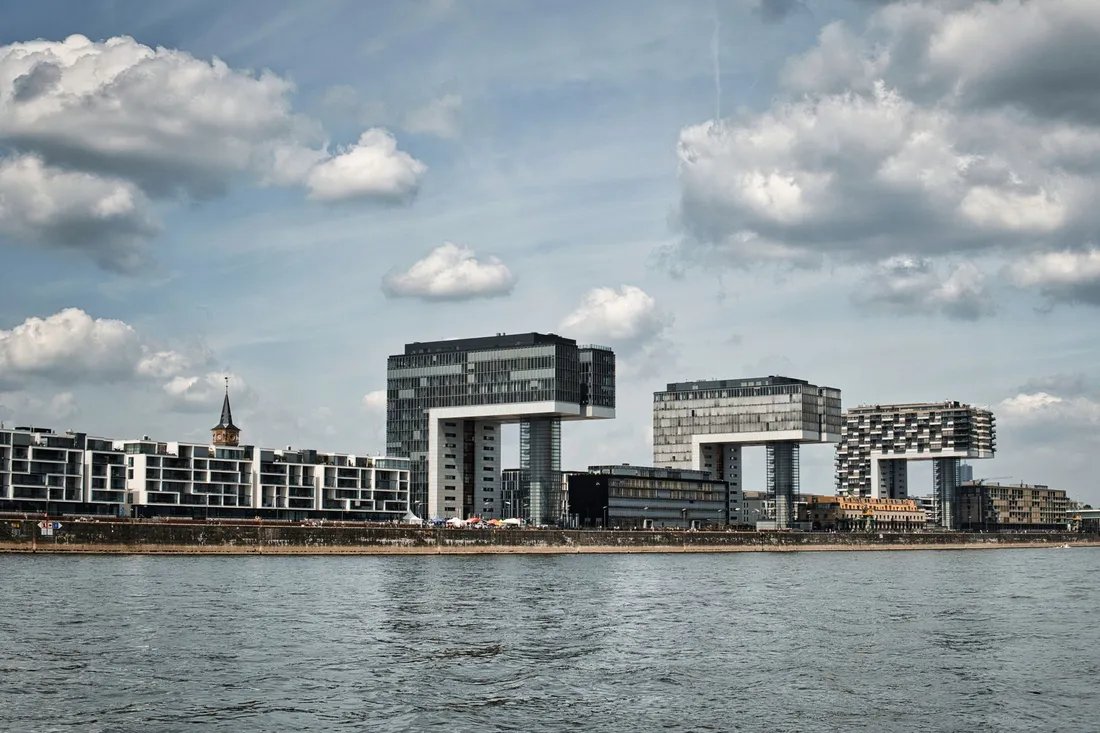Drei kranförmige Bürohochhäuser am Flussufer unter einem wolkigen Himmel