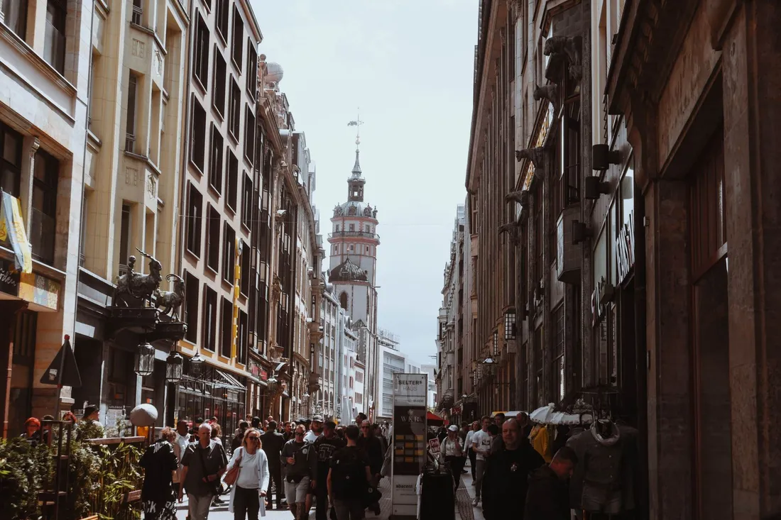 Belebte Einkaufsgasse voller Passanten, am Ende ein barocker Kirchturm mit Haube