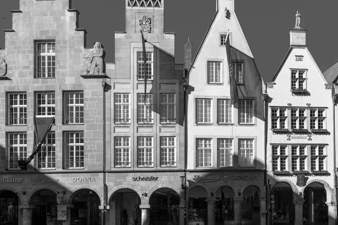 Schwarzweiße Aufnahme von Giebelhäusern mit Arkadengängen und alten Ladenschildern
