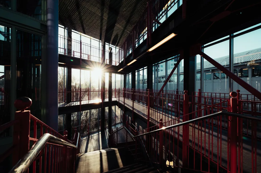 Bahnhofshalle mit roten Stahlgeländern und Treppe im Gegenlicht der tiefen Sonne