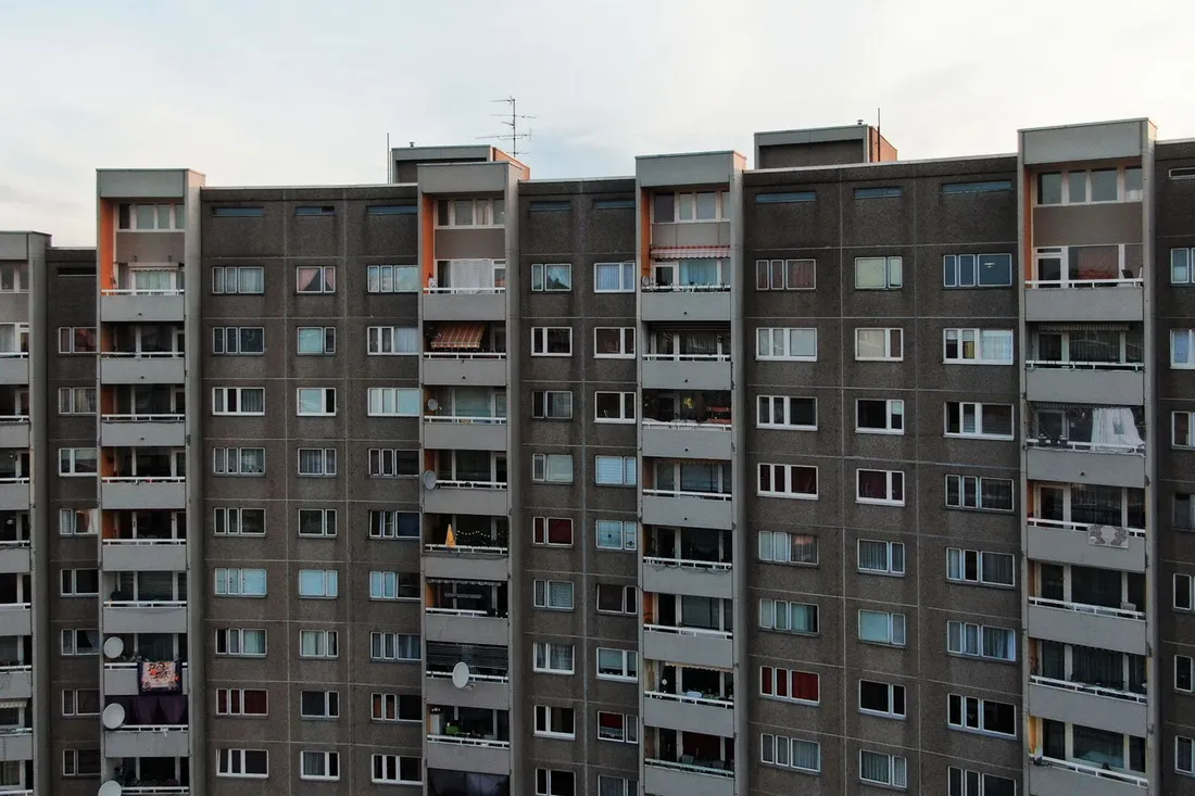 Lange Plattenbaufassade mit Balkonreihen, Satellitenschüsseln und bunten Vorhängen