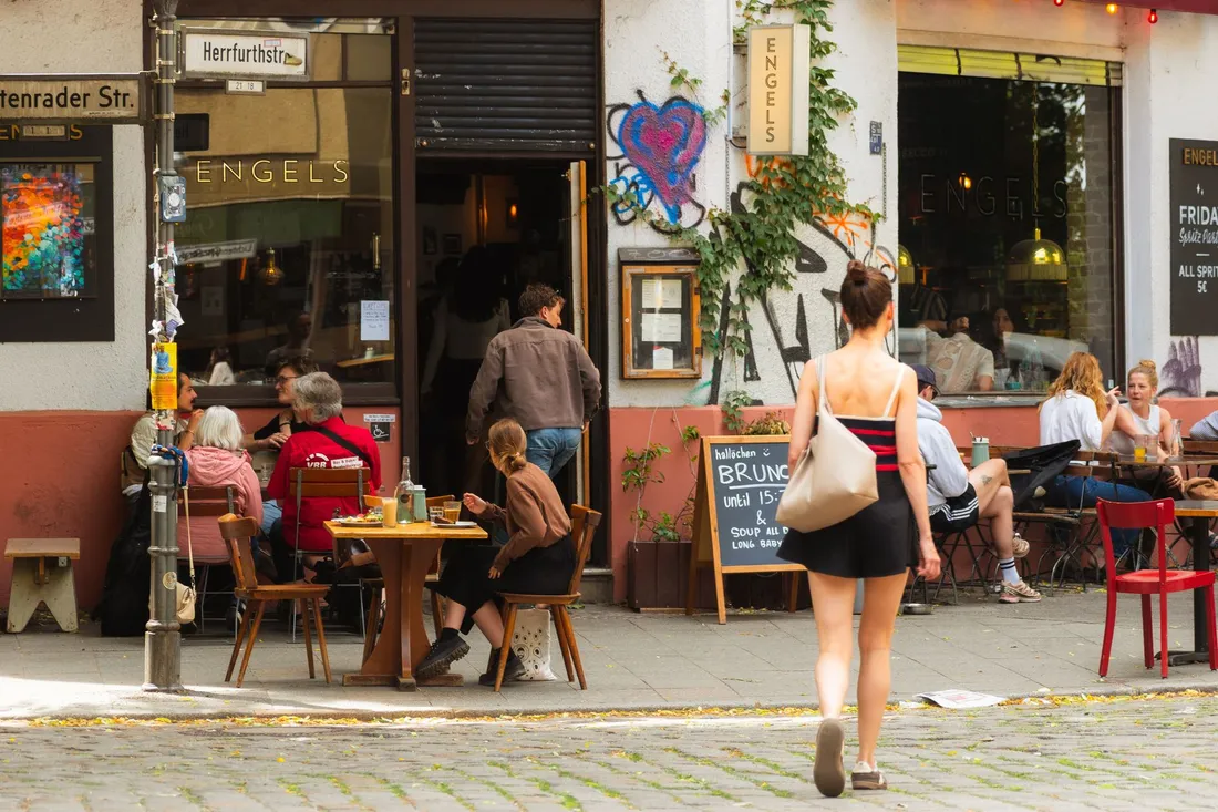 Straßencafé an einer Häuserecke, Gäste sitzen an Holztischen auf dem Bürgersteig