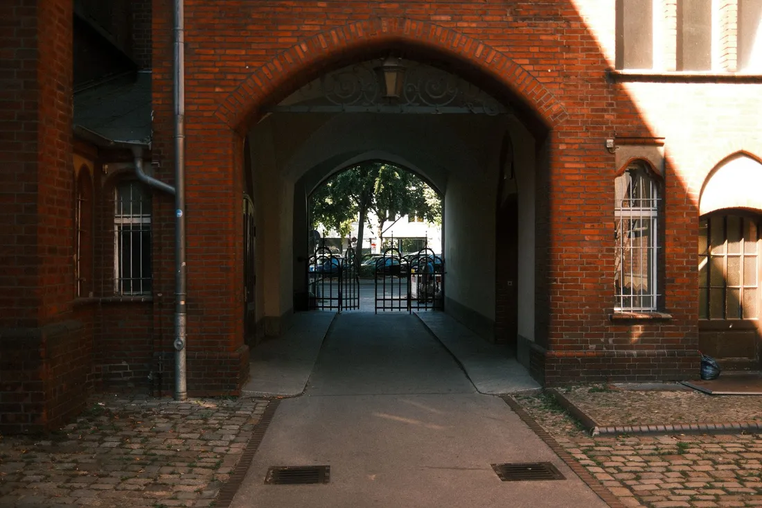 Backsteinerne Toreinfahrt mit Kopfsteinpflaster und Gittertor zum begrünten Hinterhof