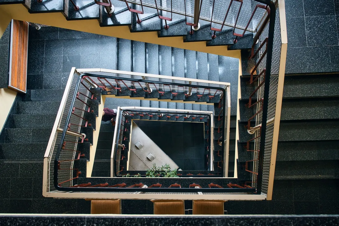 Blick von oben in ein Treppenhaus mit Terrazzostufen und roten Geländerstäben