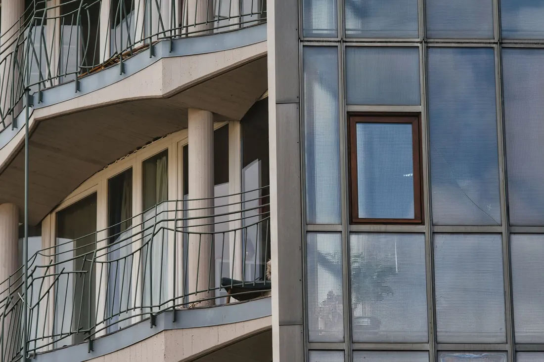 Geschwungene Balkone eines hellen Wohnhauses neben einer gerasterten Glasfassade